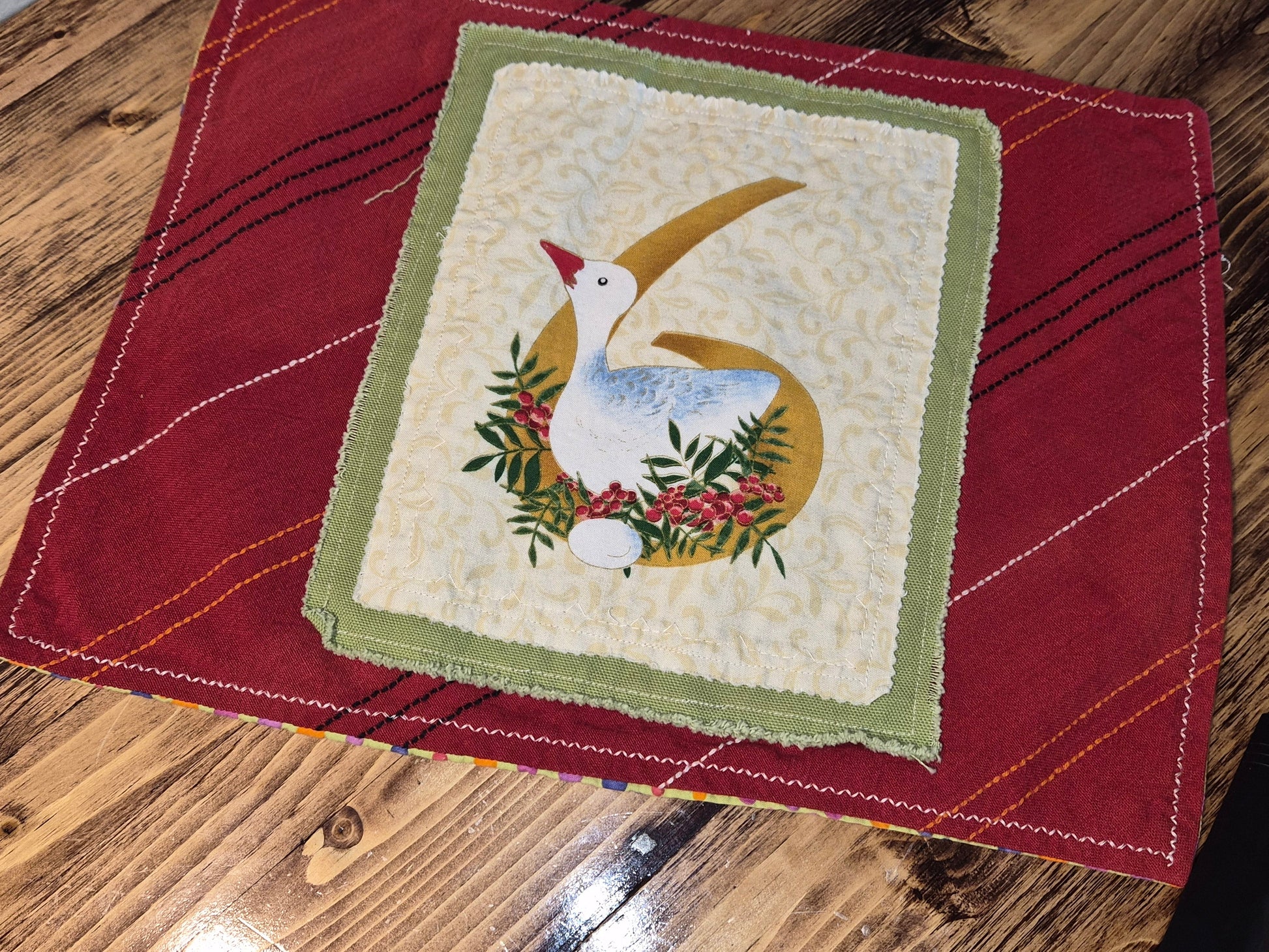 Quilted square with a goose design on a red fabric background