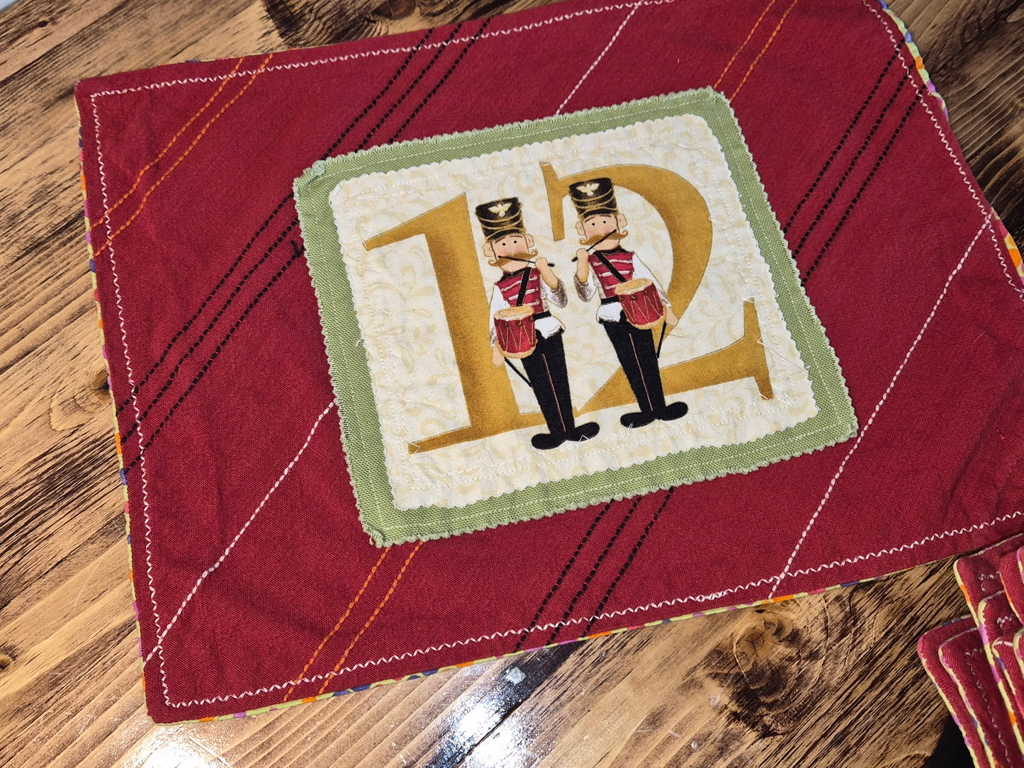Red quilted fabric with a decorative square featuring two nutcrackers and the letter 'D'.