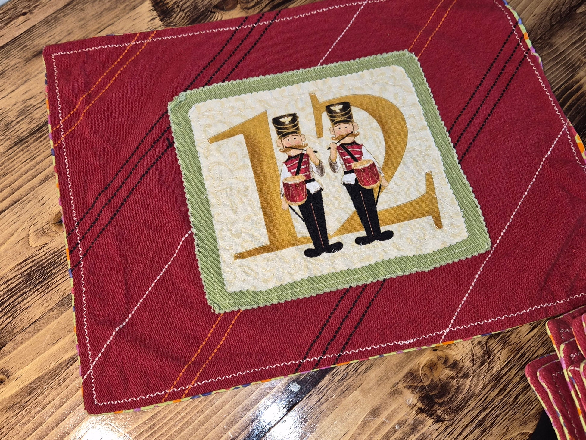 Red quilted fabric with a decorative square featuring two nutcrackers and the letter 'D'.