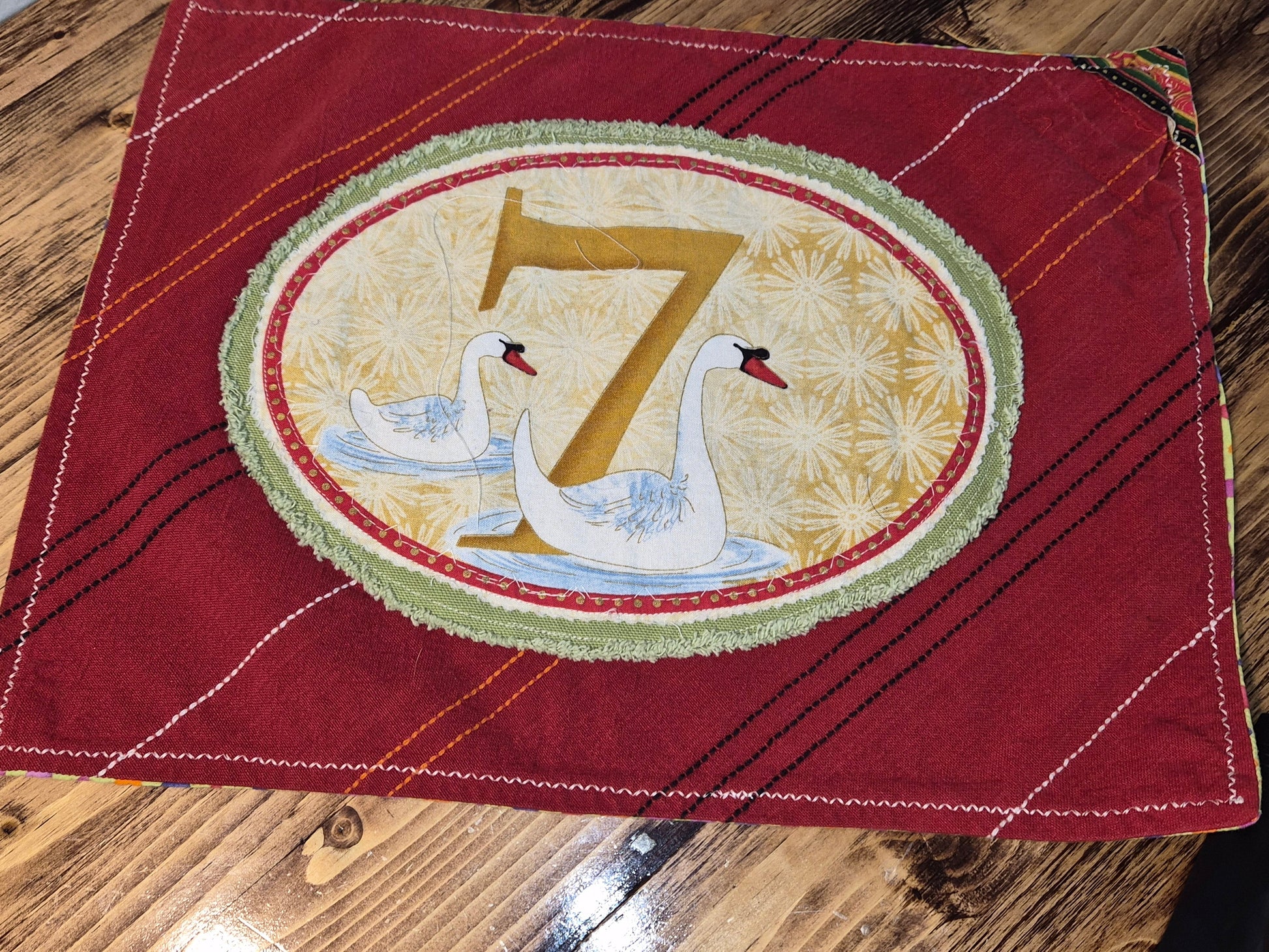 Red fabric with a decorative patch featuring swans and the number 7 on a wooden surface.