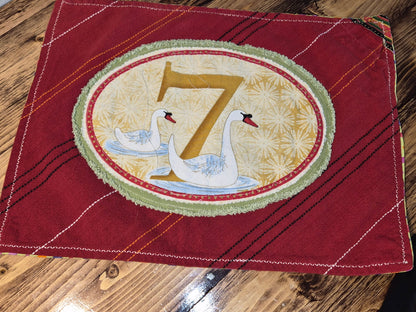 Red fabric with a decorative patch featuring swans and the number 7 on a wooden surface.