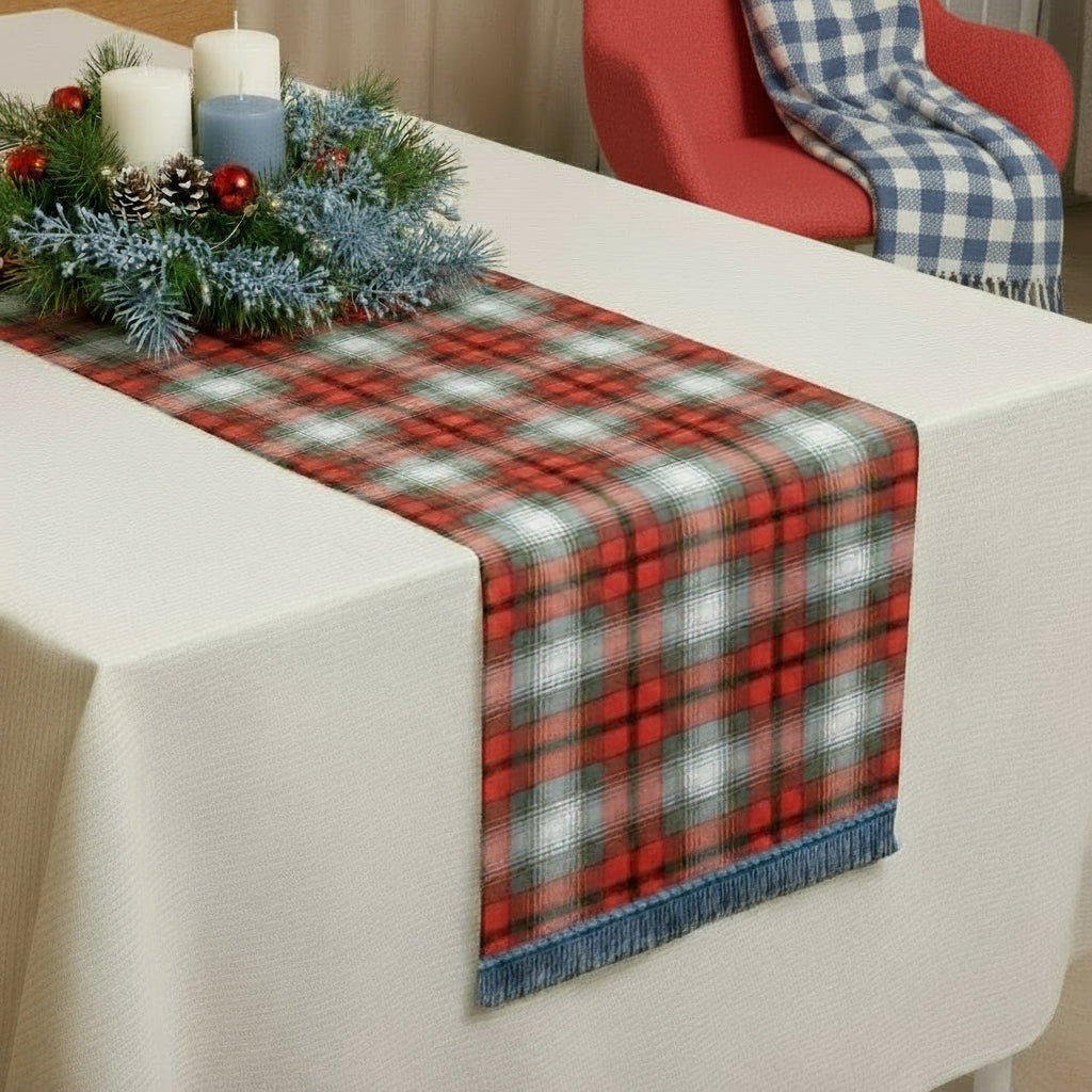 Red, white, grey, gold, and black tartan table runner on a white table with a Christmas centerpiece.
